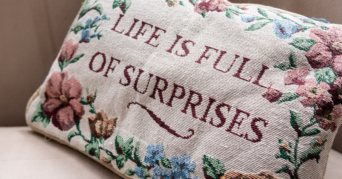 header image depicting a pillow cross-stiched with the sentence, 'Life is Full of Surprises'